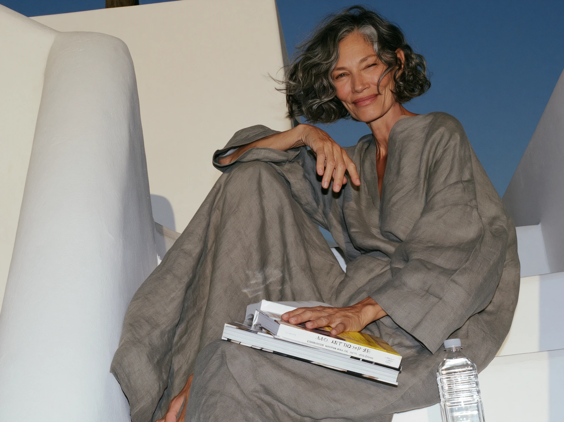 Silver-haired woman resting on white steps, smiling in the sun